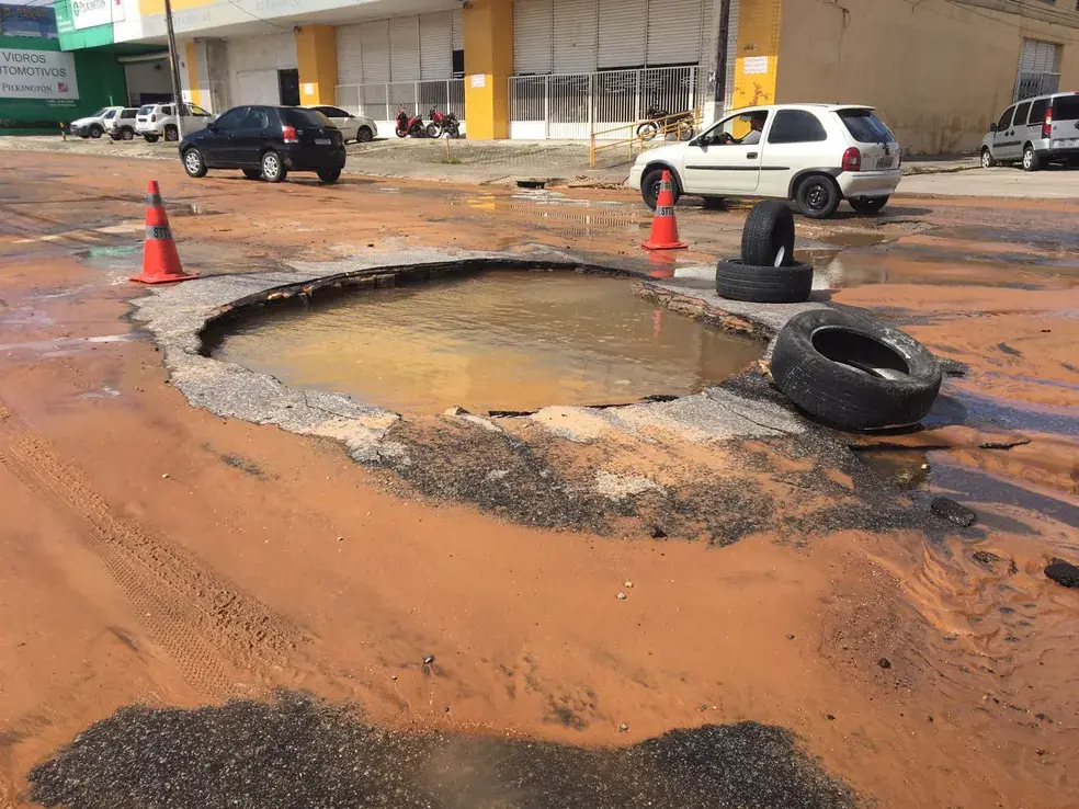 Buraco cheio de água barrenta, cercado por cones e pneus