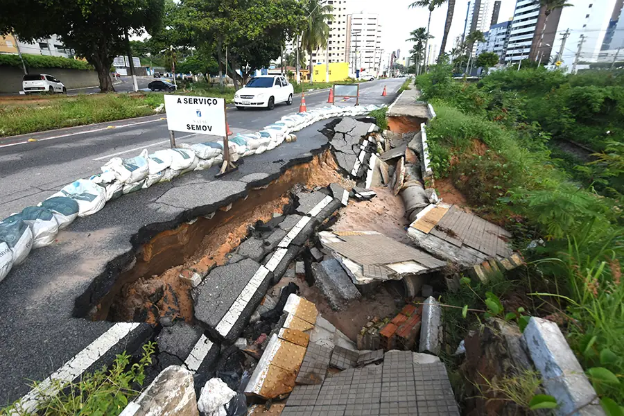 Pista e calçada desabadas, com sacos de areia na beira