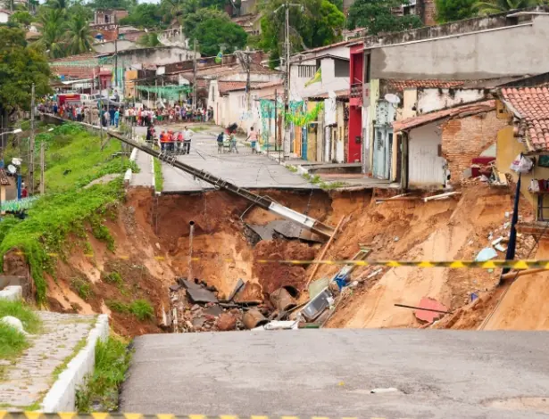 Rua desabada ao lado de casas, com moradores olhando